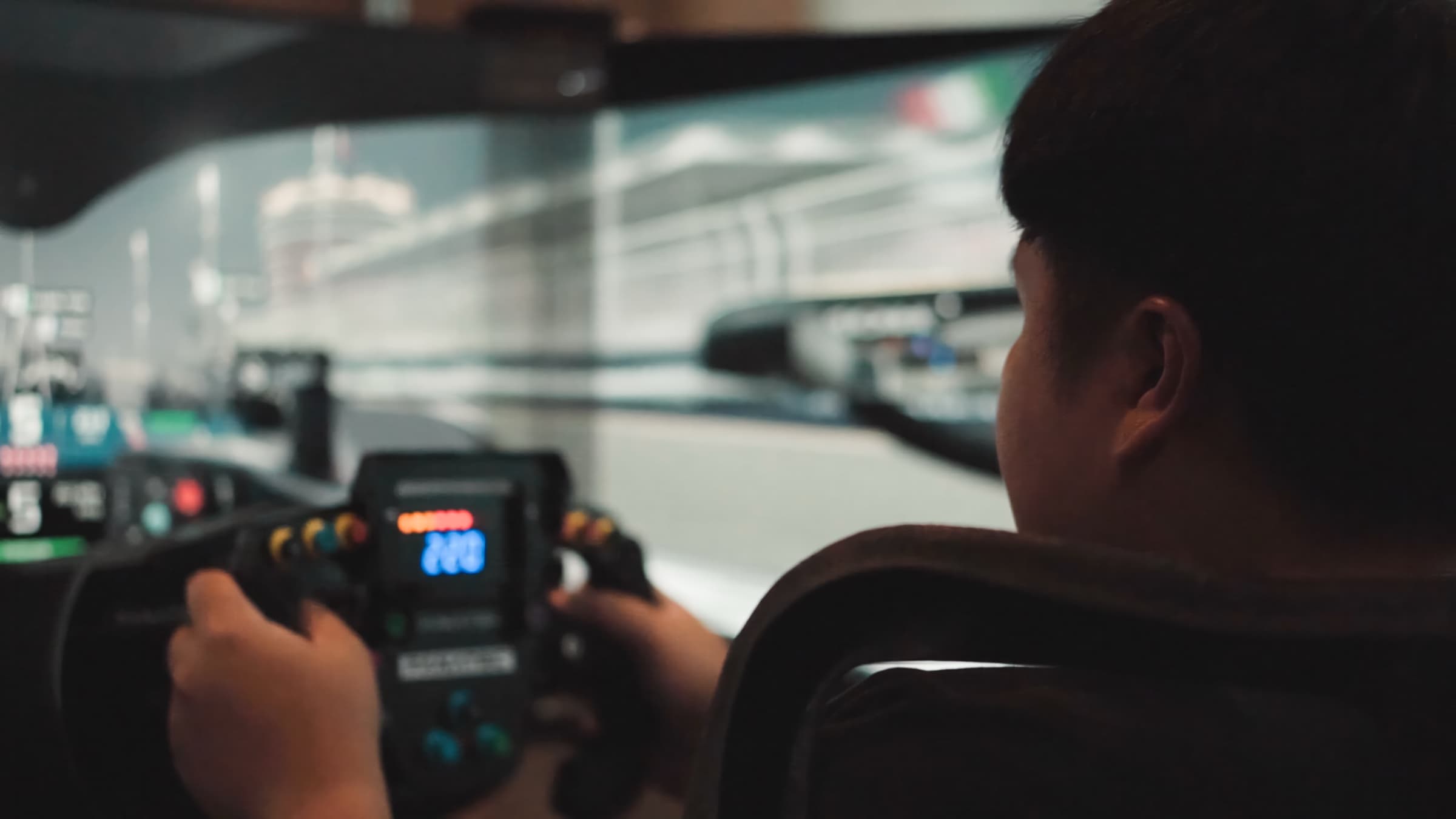 Over-the-shoulder view of a sim racer at a formula-style wheel with an in-wheel telemetry display